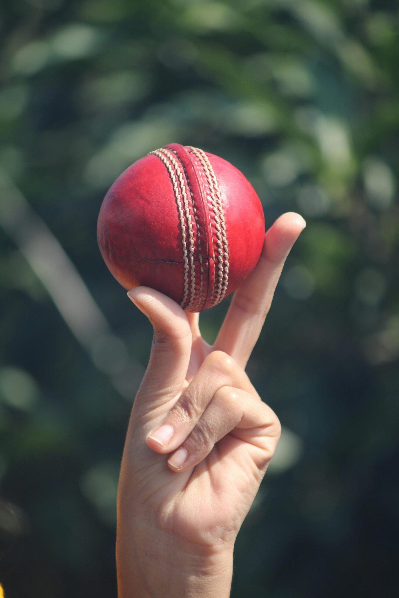 A red cricket ball balanced on fingers outdoors in Jabalpur, India.
